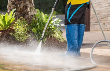 This image shows a man power washing the driveway of a house.