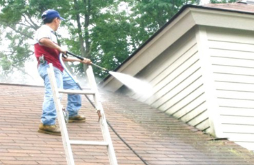 This image shows a man power washing the roof of a house.