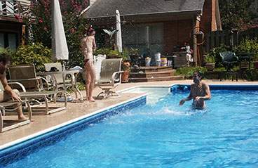 This image shows a woman standing beside a pool while talking to a man in a pool.